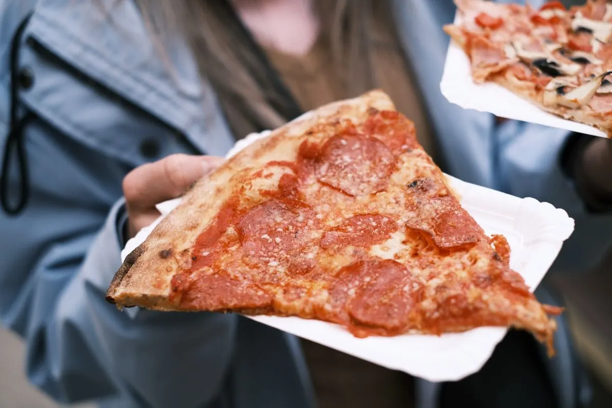 Ruka drží kousek pepperoni pizzy na tácku